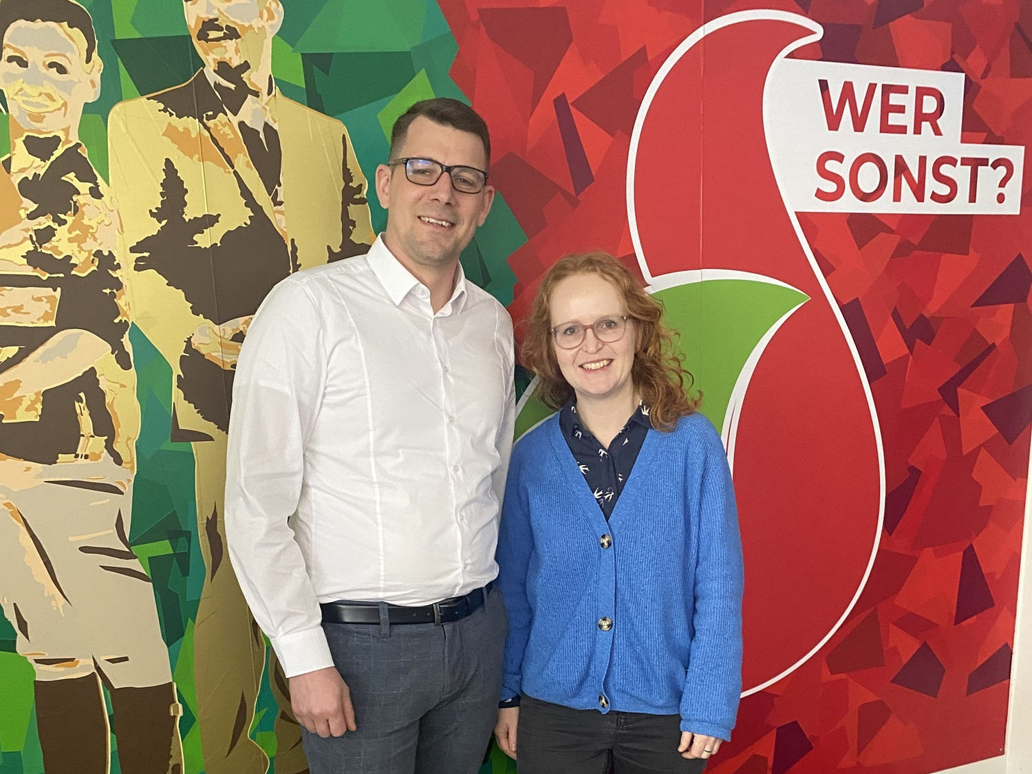 Ein Mann und eine Frau stehen lächelnd vor einer bunten Wand.