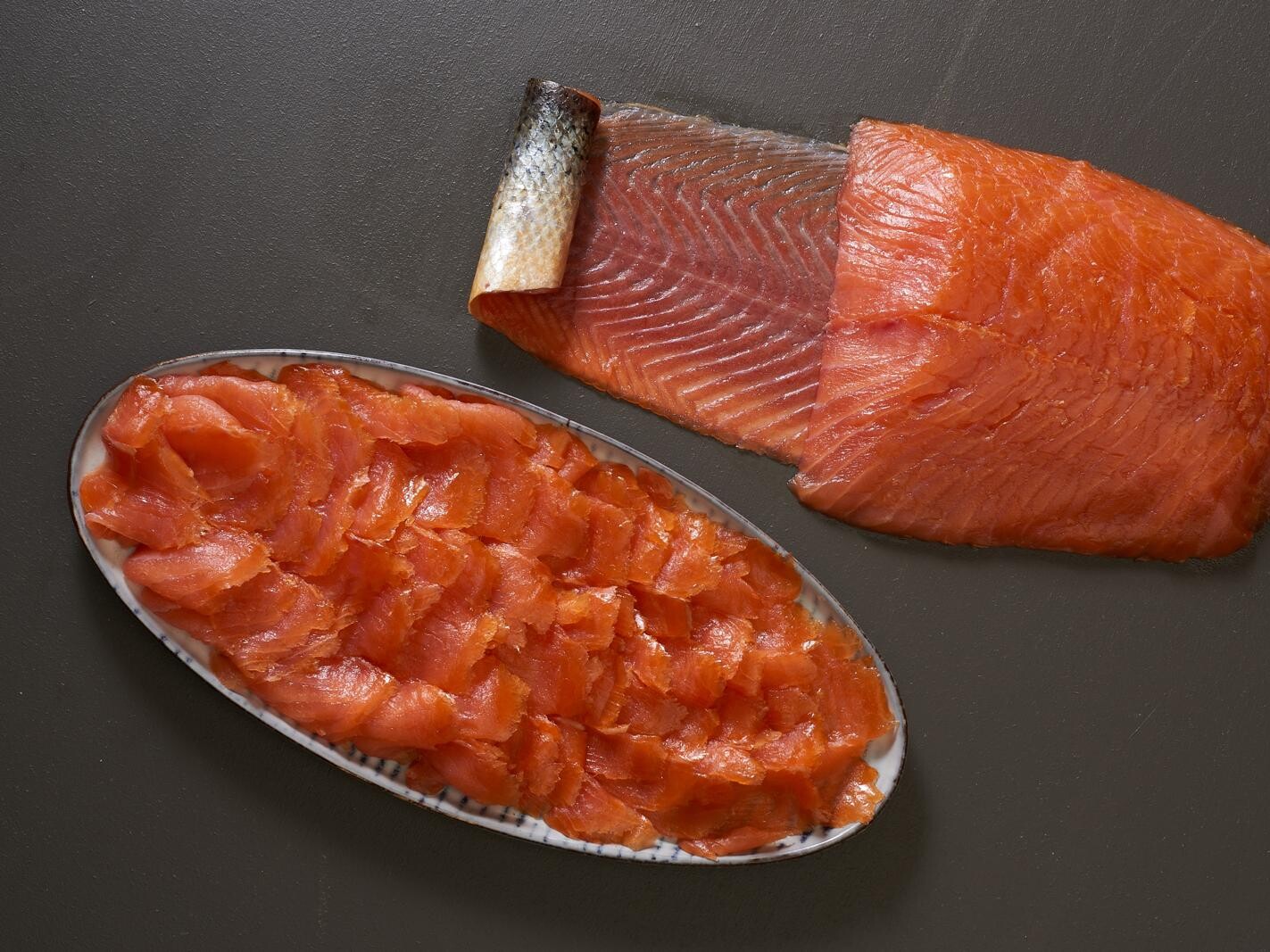 Räucherlachs auf einer Platte, daneben eine Lachsseite