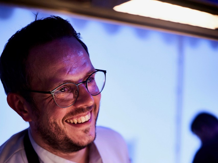 Ein Mann mit Brille lächelt ein Tellergericht an.