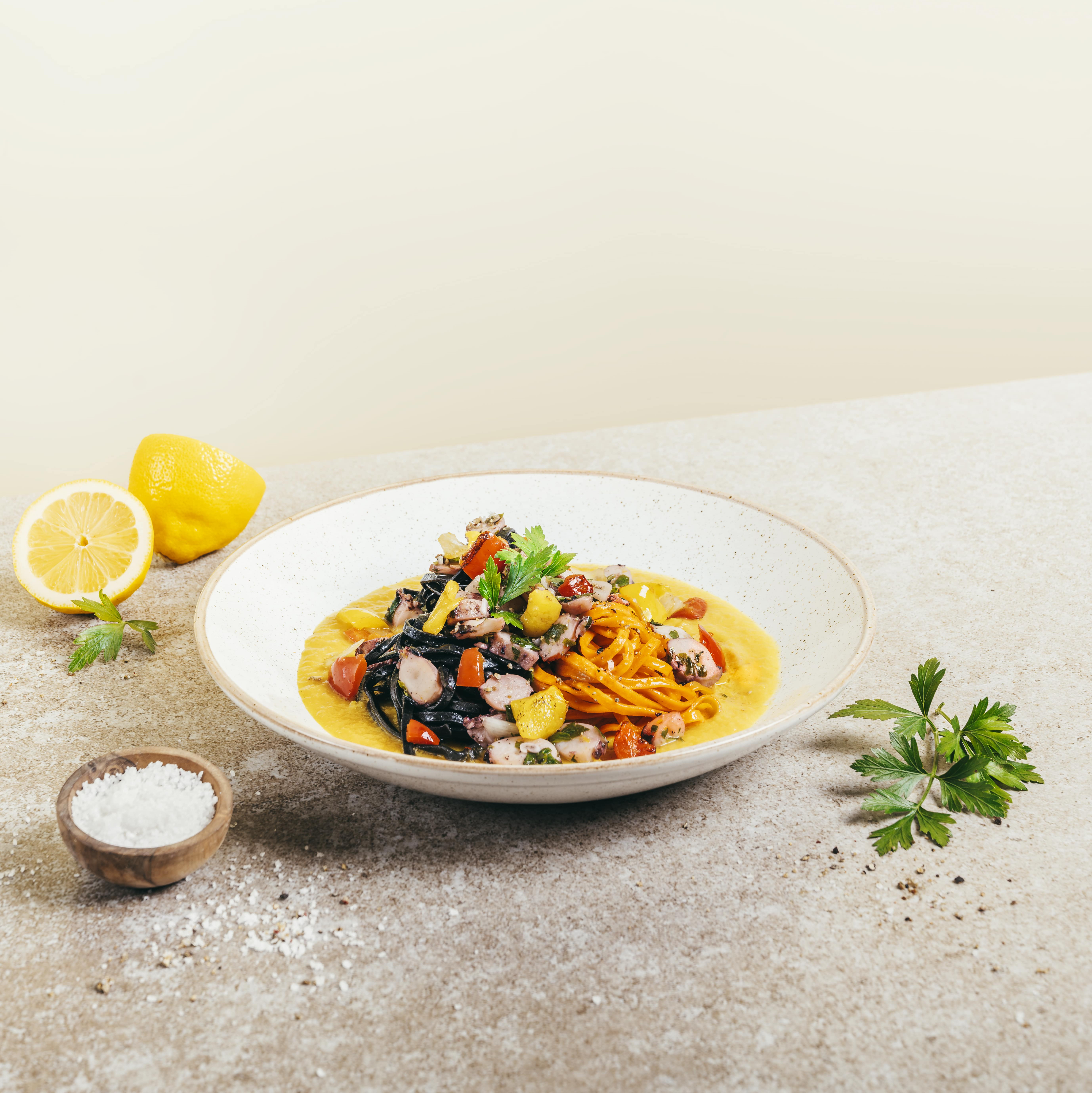 Ein Teller mit einem Pastagericht mit Riesenkalmar und Paprikawürfeln auf einem Tisch.